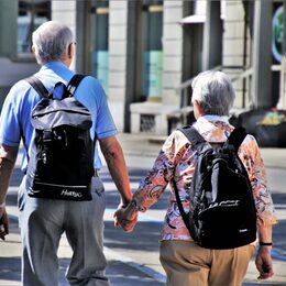 Zwei ältere Menschen mit Tagesrucksäcken gehen Hand in Hand spazieren