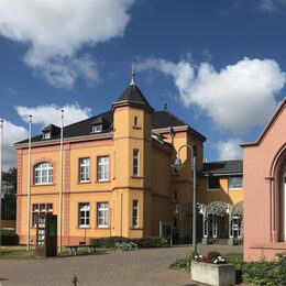 Links im Bild das Rathaus Vettweiss davor rechts eine Kapelle mit Kruzifix